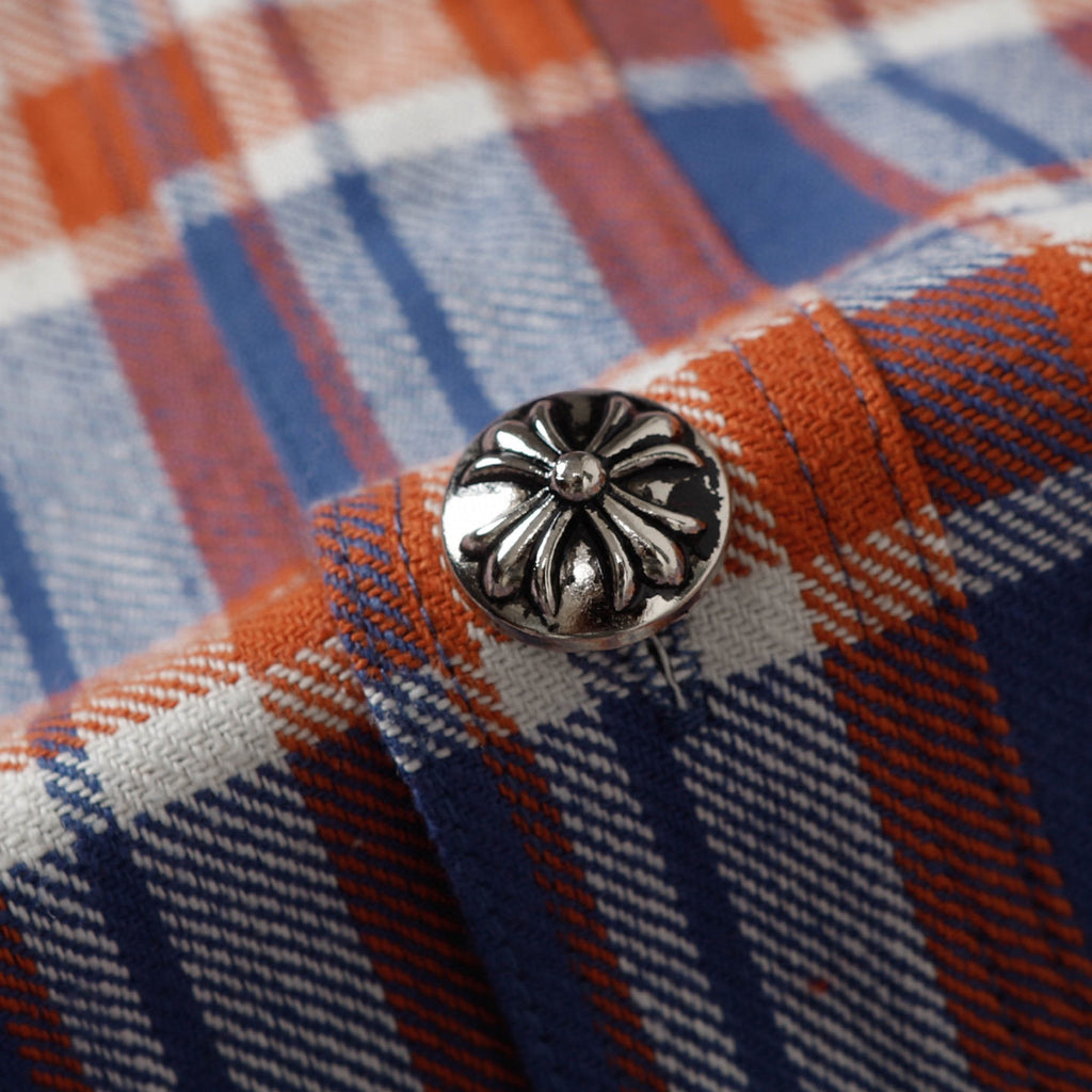 Metal-style shirt button with ornate floral design on plaid fabric.