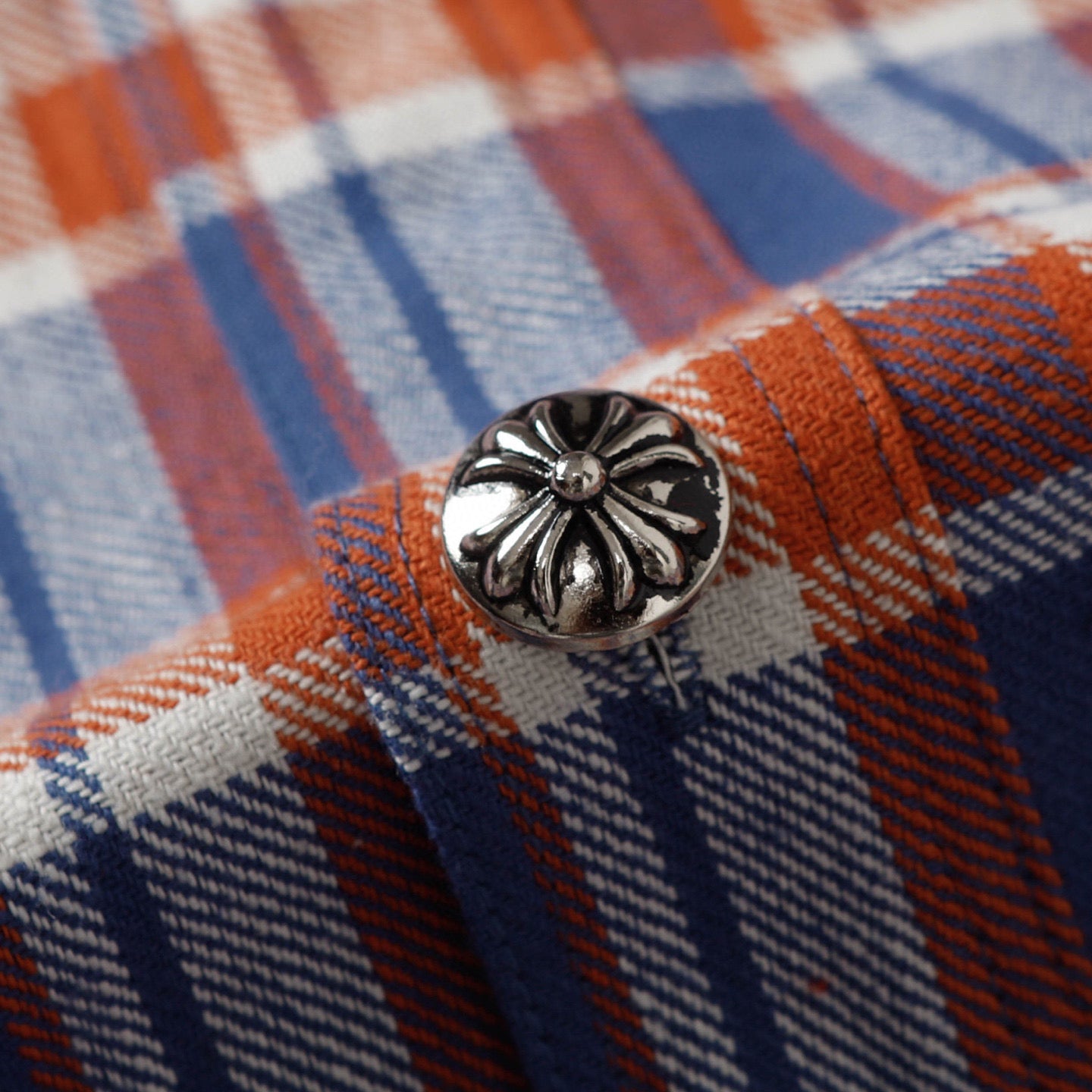 Metal-style shirt button with ornate floral design on plaid fabric.