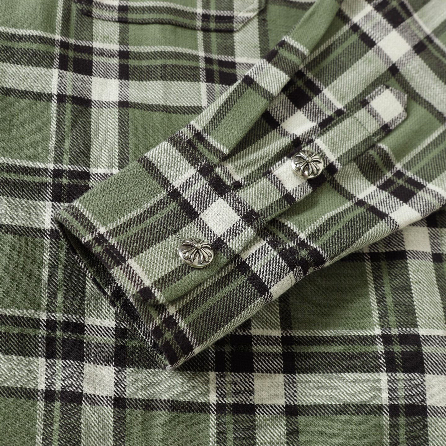 Cuff detail of plaid shirt with button and metal embellishments in green with black checks
