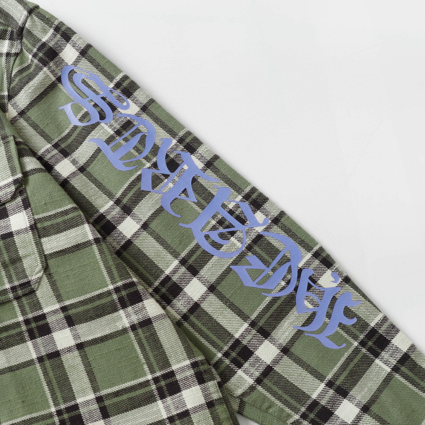 Long-sleeve plaid shirt sleeve with blue script text over green, black, and white checks