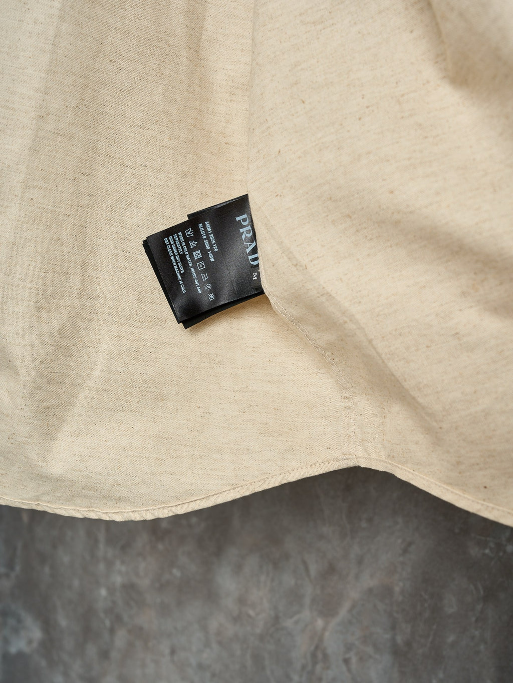 Cream long-sleeve button-up shirt hem with attached product tag