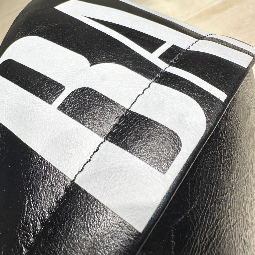 Balenciaga bag close-up of large white logo print on black leather panel.