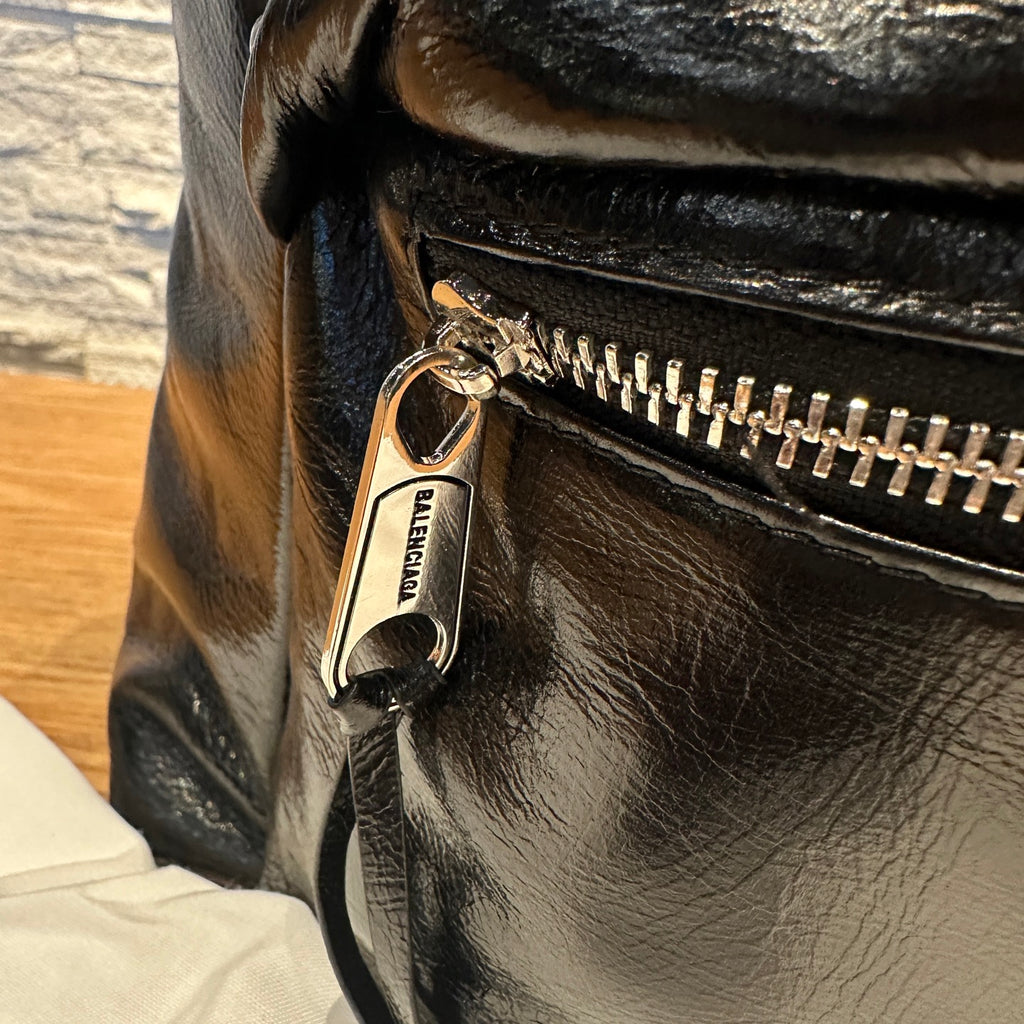 Balenciaga bag close-up of metal zipper pull on black leather with logo charm.