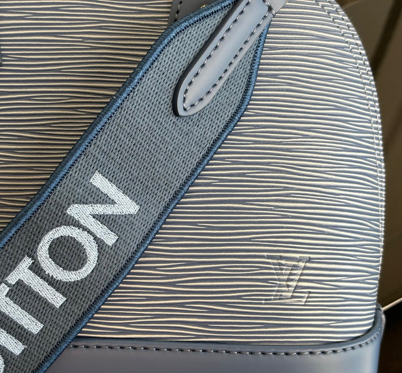 Blue Louis Vuitton strap close-up with bold lettering on textured material.