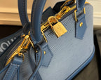 Blue Louis Vuitton handbag close-up of gold padlock charm and zipper hardware.