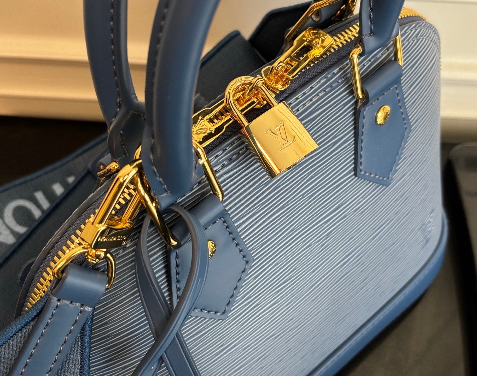 Blue Louis Vuitton handbag close-up of gold padlock charm and zipper hardware.