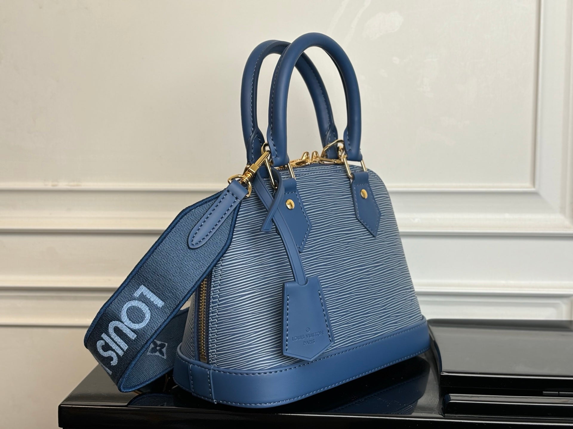 Blue Louis Vuitton handbag angled view with top handles and long crossbody strap.