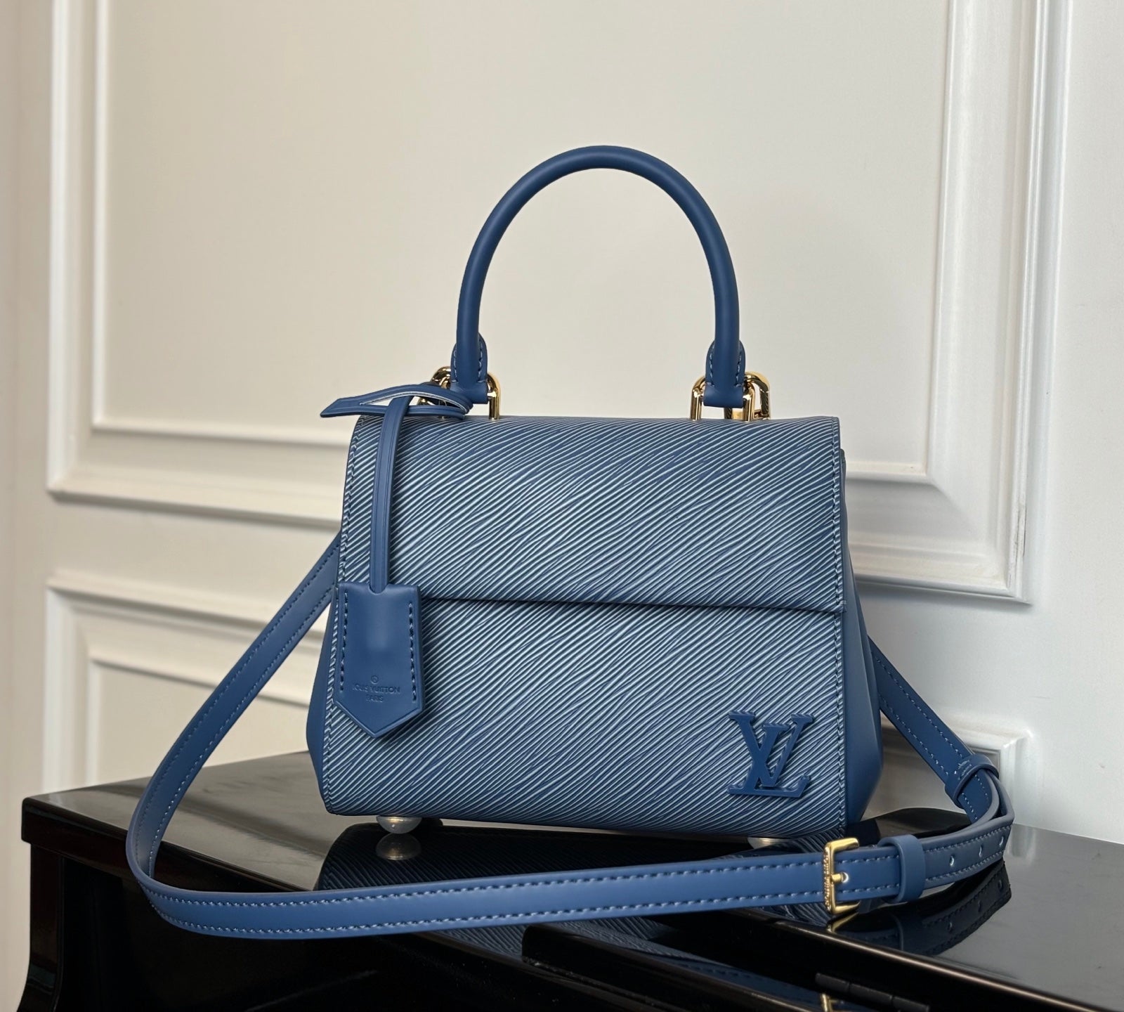 Blue textured leather handbag with top handle, front flap, and gold-tone hardware.