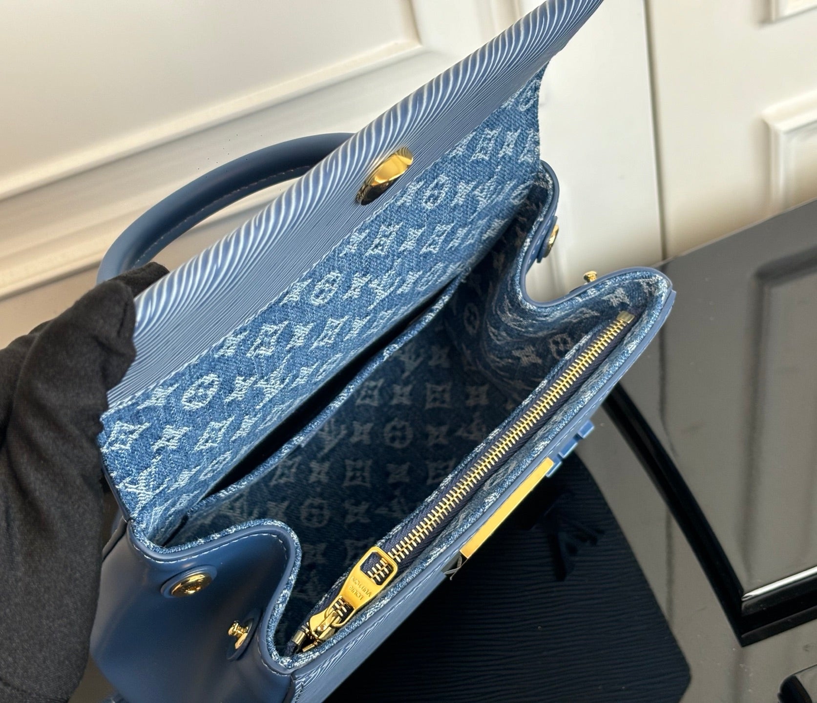Blue handbag open to show monogram lining and zipper, with gold hardware.