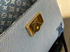 Blue textured handbag with gold logo plaque and gold button hardware detail.