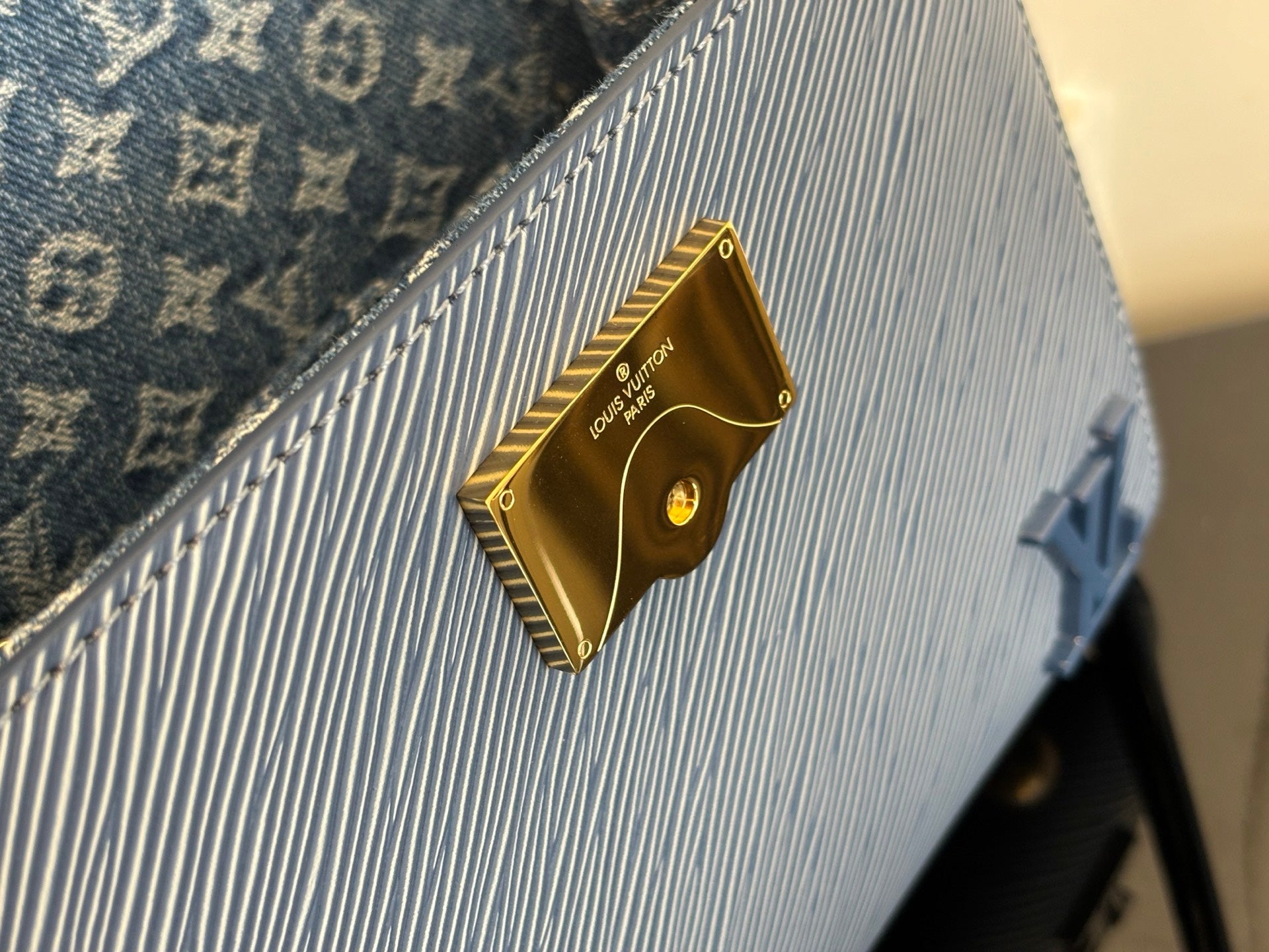 Blue textured handbag with gold logo plaque and gold button hardware detail.