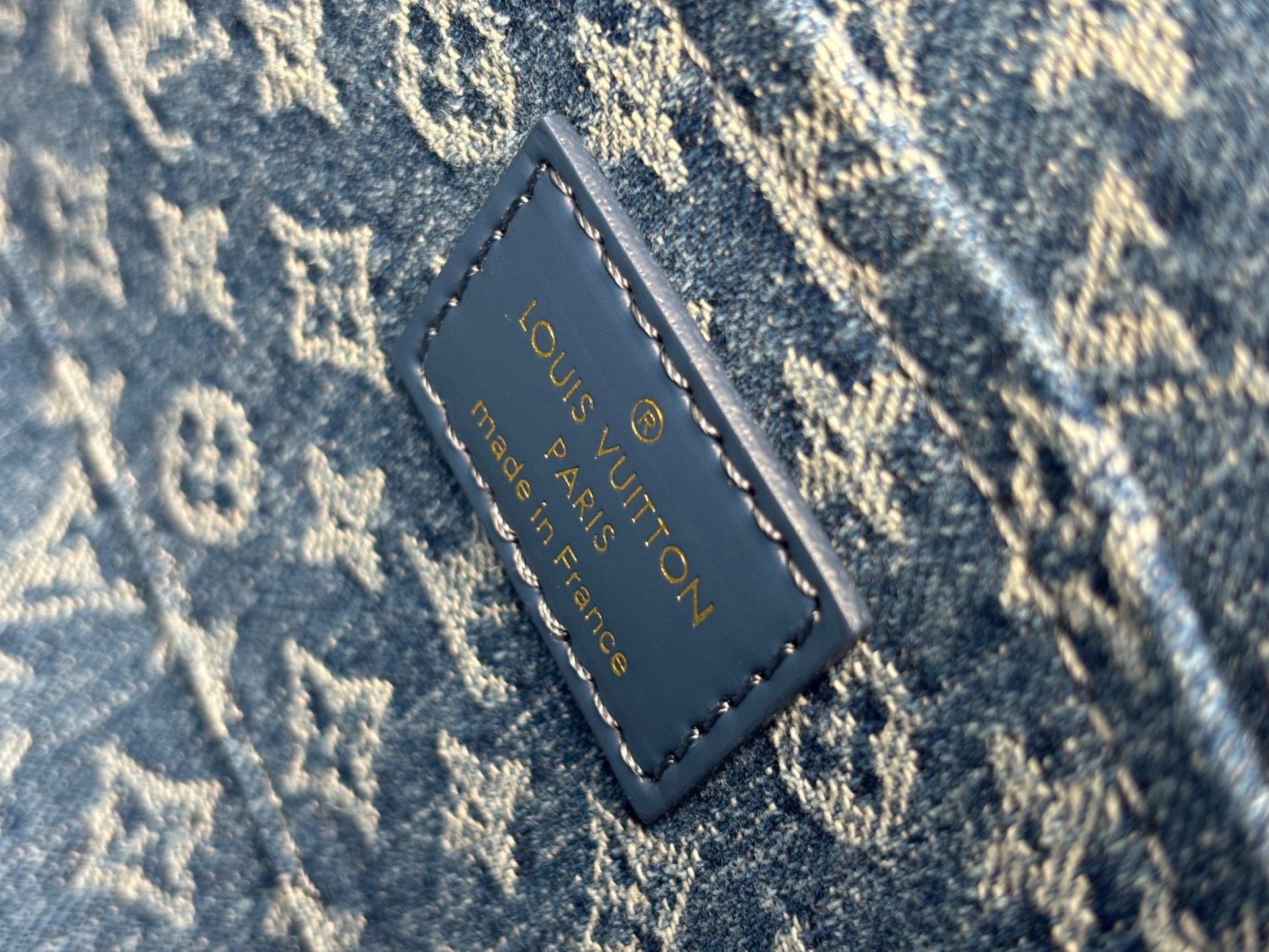 Blue leather logo patch with 'Louis Vuitton' text and stitched border.