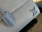 Blue textured leather handbag close-up with gold logo and stitched leather tag.