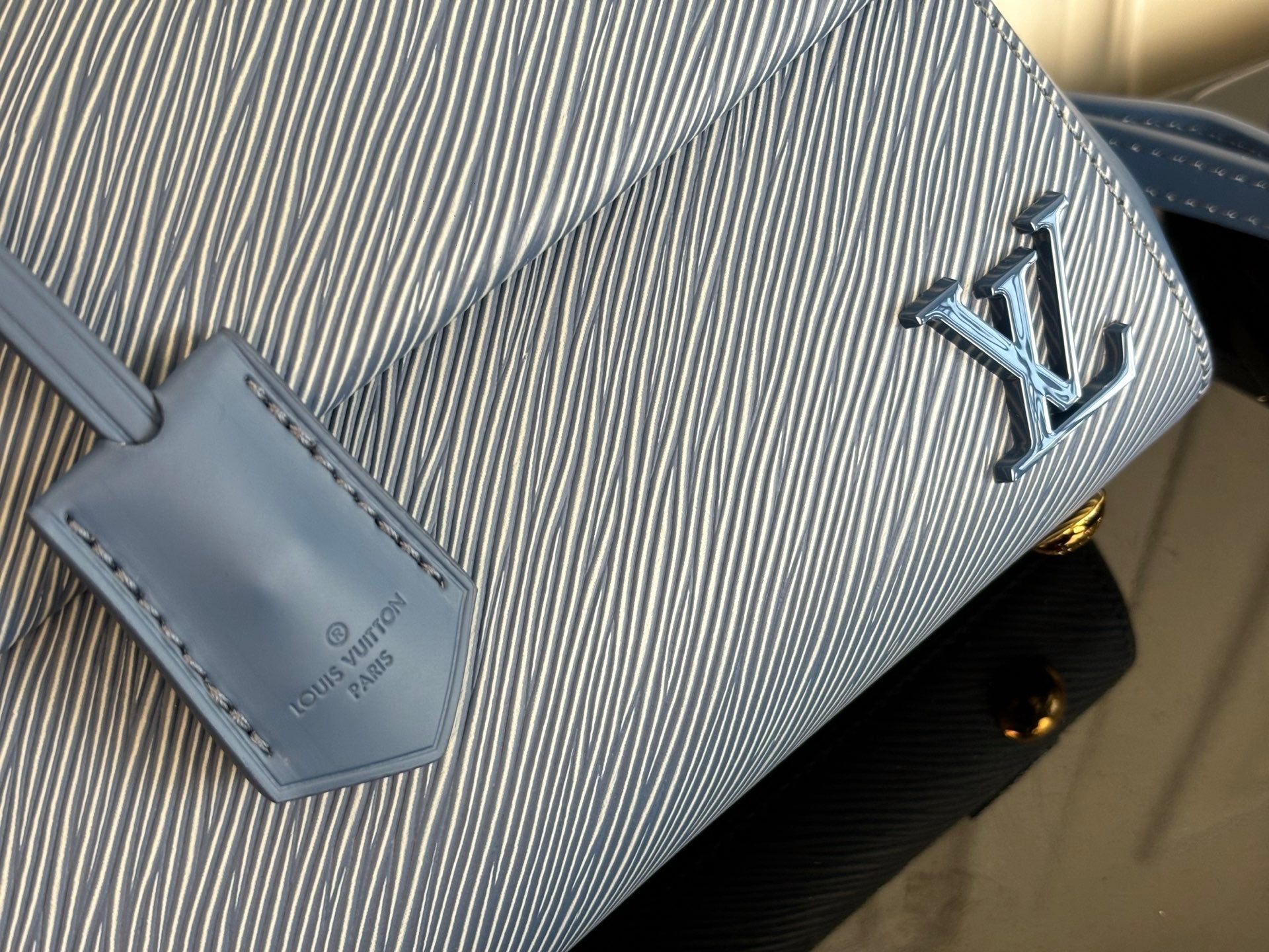 Blue textured leather handbag close-up with gold logo and stitched leather tag.