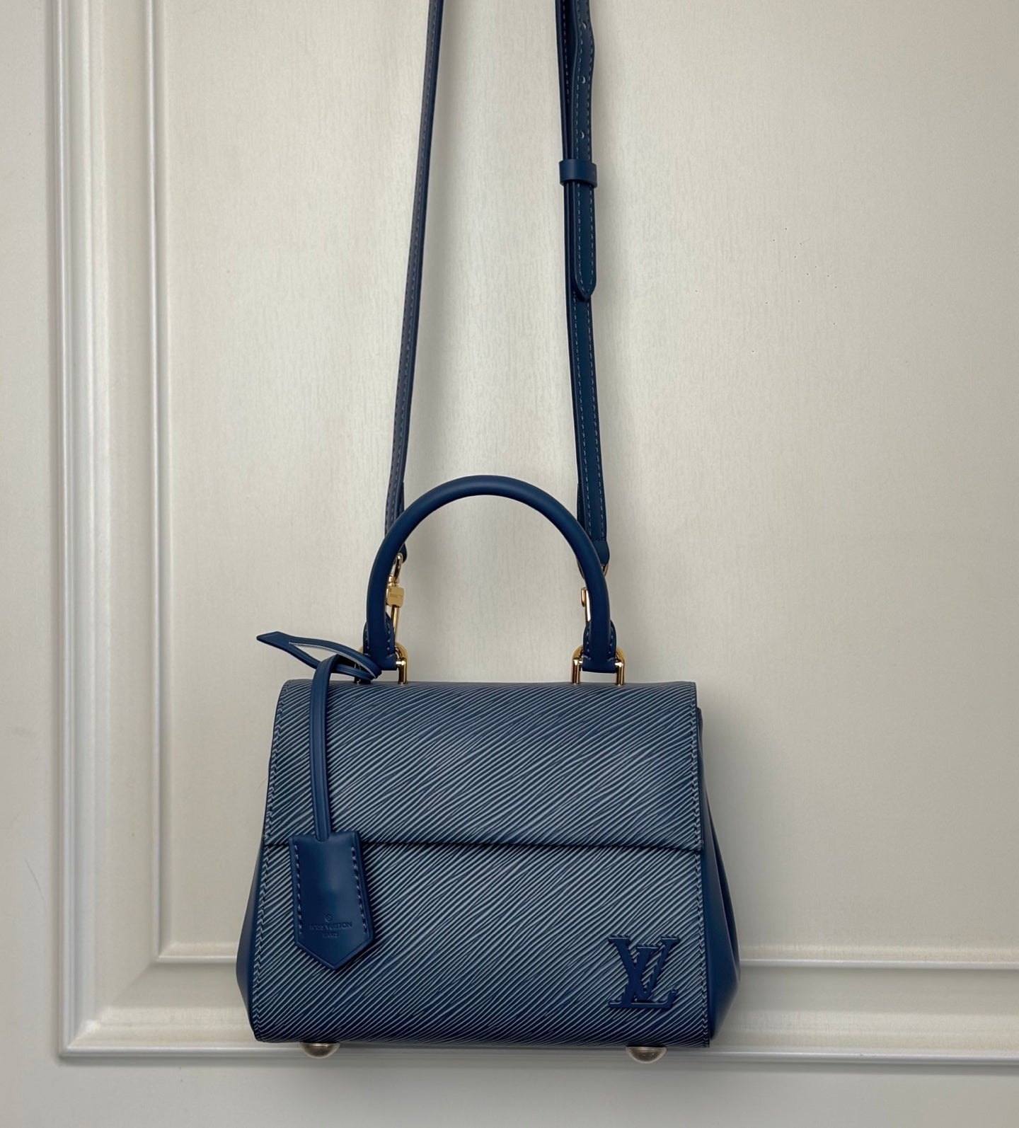 Blue structured handbag with top handle and long shoulder strap, gold-tone hardware.
