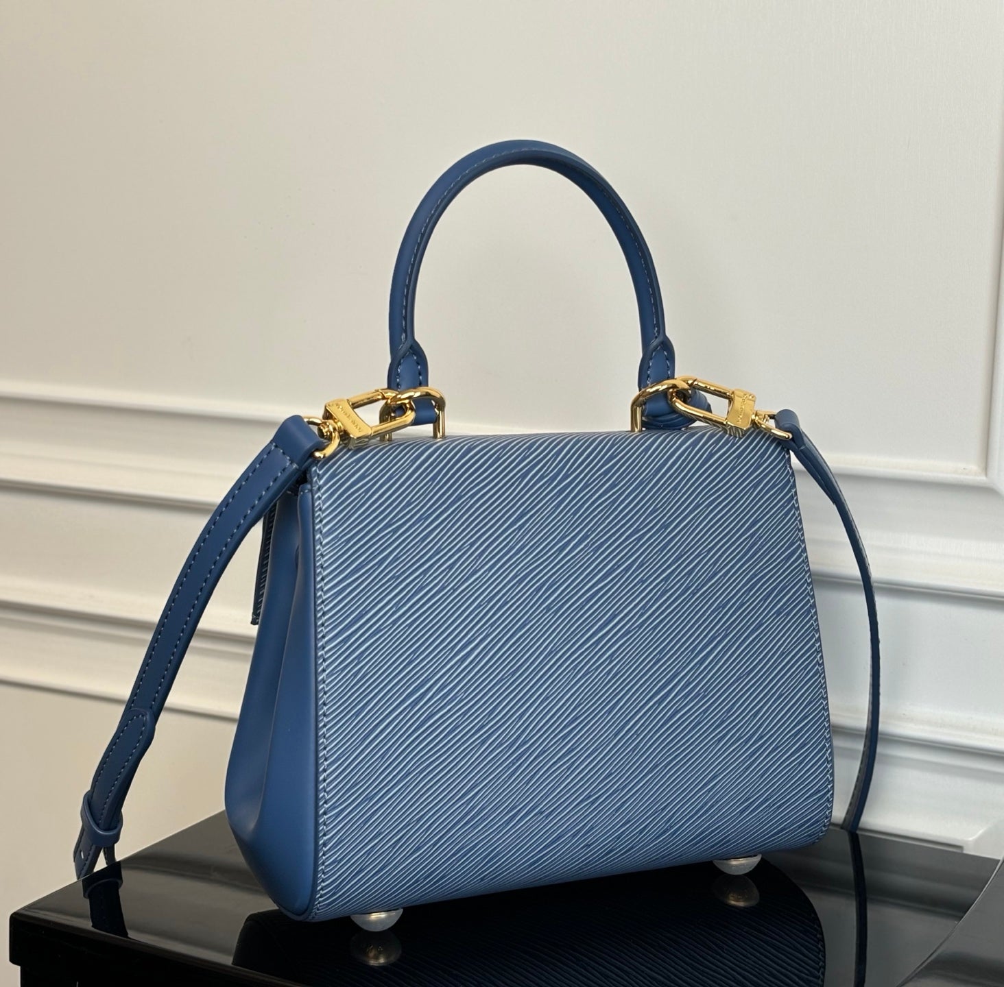 Blue textured handbag with top handles and shoulder strap, gold clasp hardware.