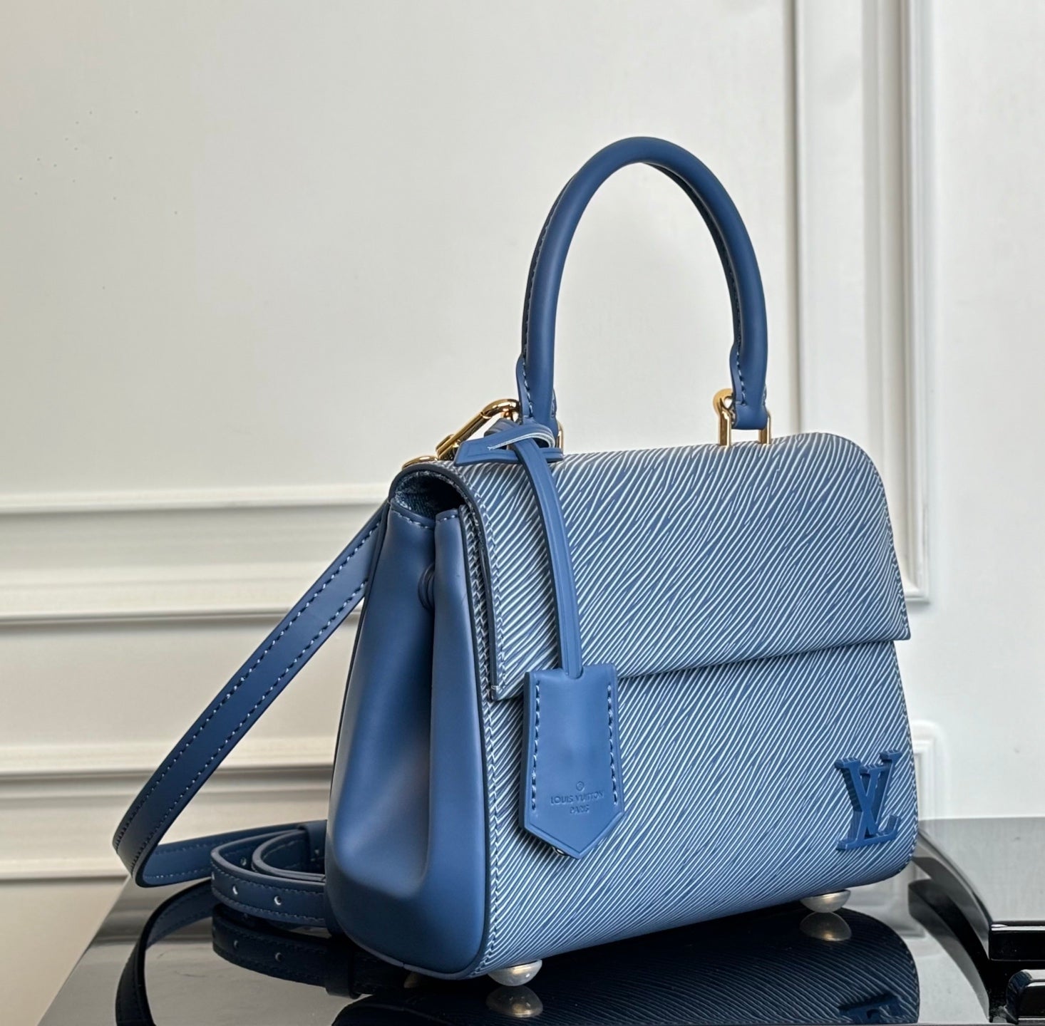 Blue structured handbag with shoulder strap, front flap, and gold-tone hardware.