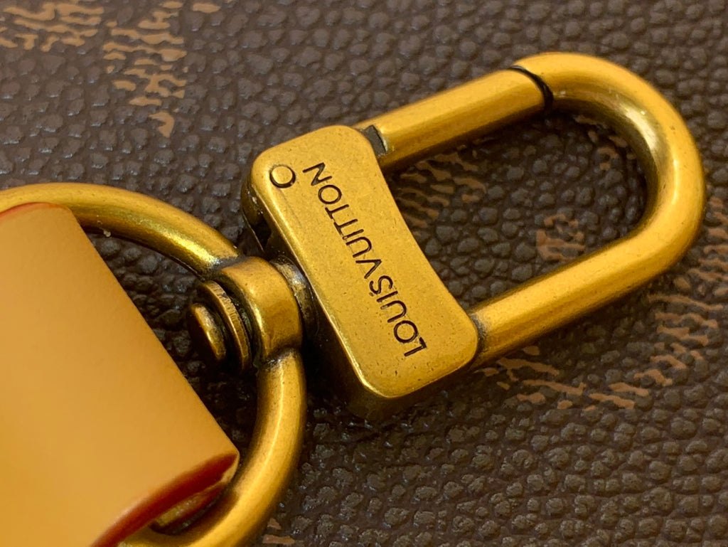 Gold padlock charm labeled Louis Vuitton on monogram canvas bag