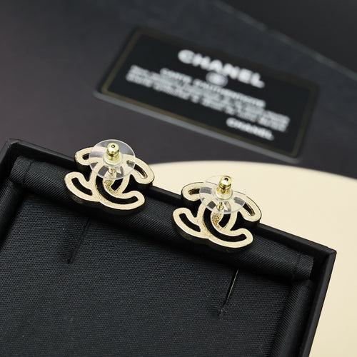 Chanel earrings with gold-tone CC logo and green pin detail on black fabric backing