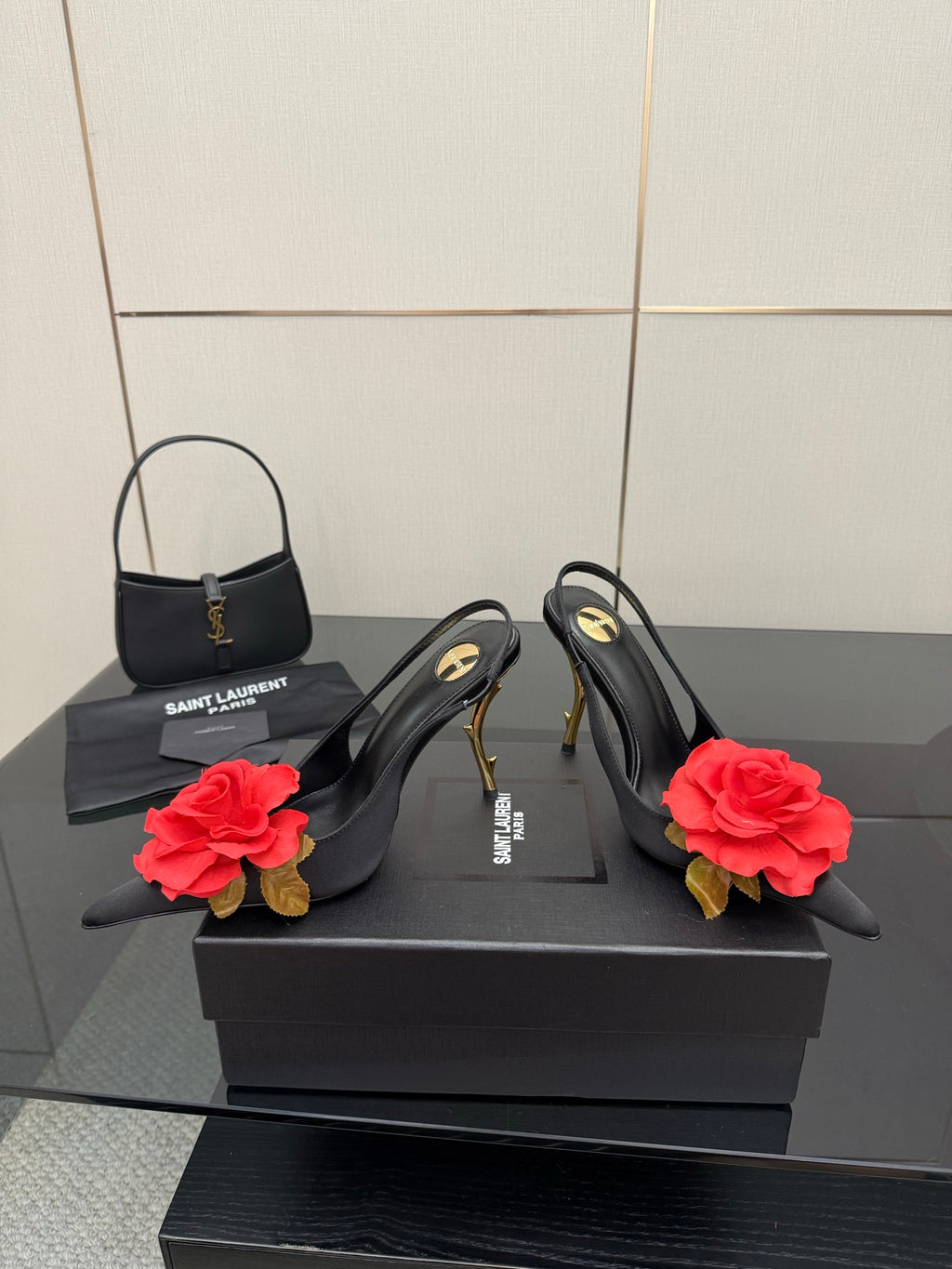 Black slingback heels with red rose clips and gold stiletto heels beside mini handbag