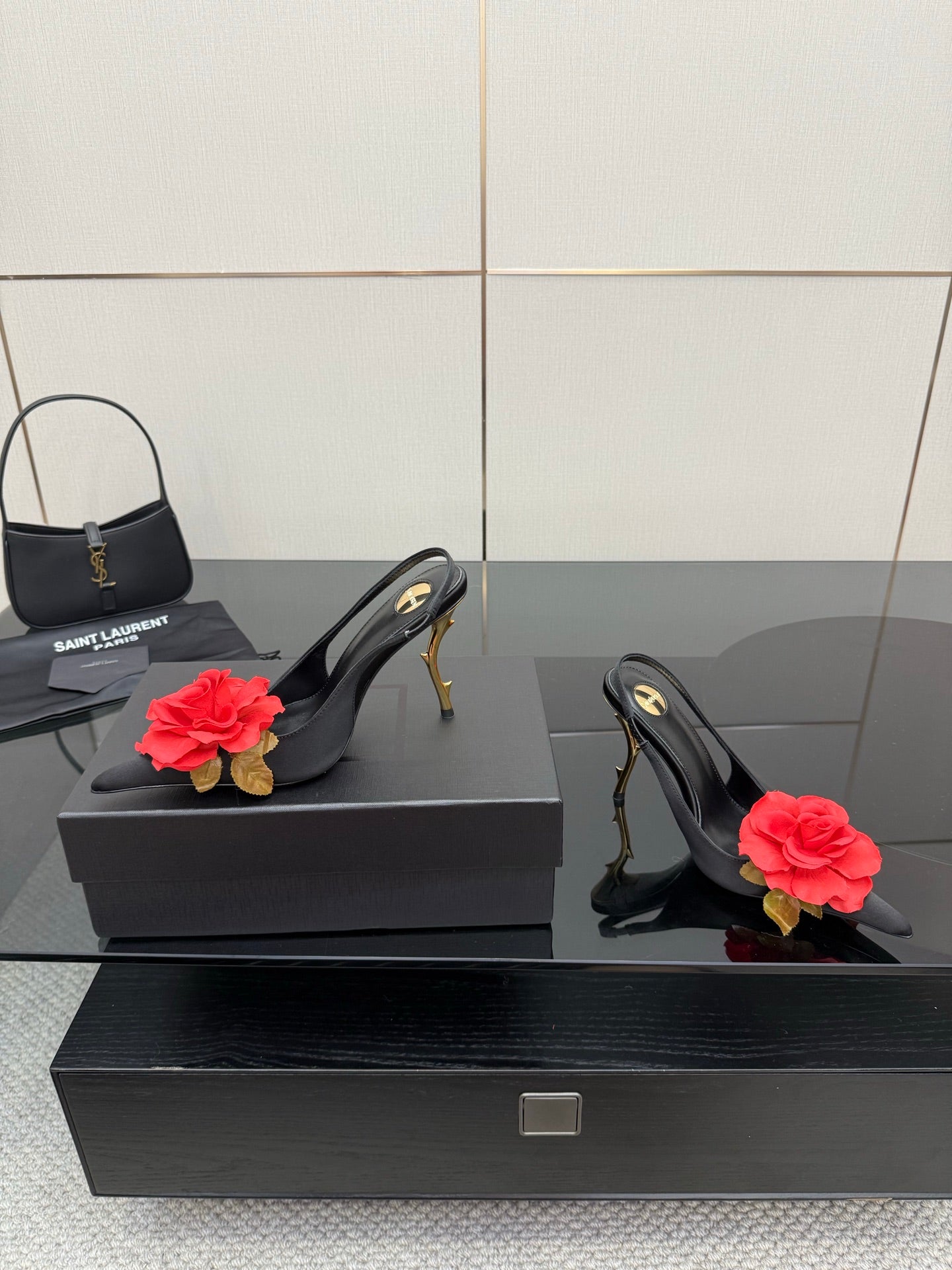 Black slingback heels with red rose clips and gold stiletto heels next to mini handbag
