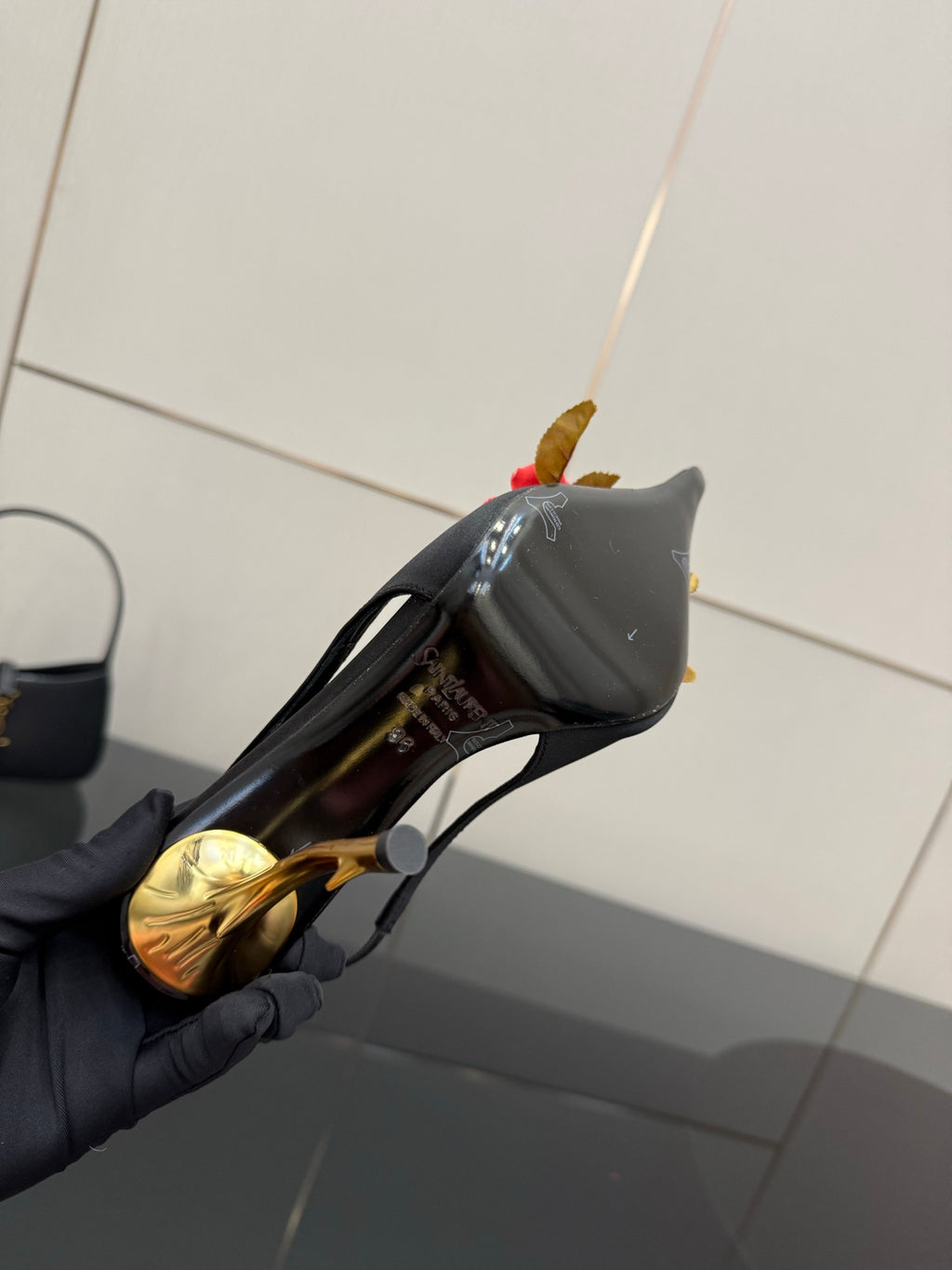 Black mini handbag with gold zipper beside a black slingback heel and red rose