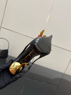 Black mini handbag with gold zipper beside a black slingback heel and red rose