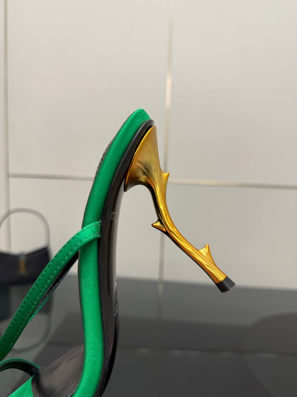 Close-up of green sandal heel with gold-toned stiletto and black heel border