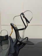 Black strappy sandal with ankle sling strap and gold-tone stiletto heel detail.