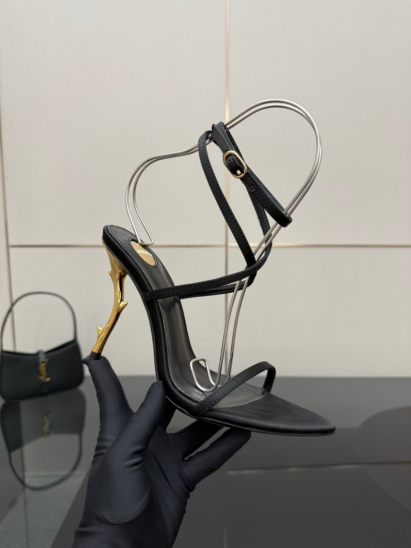 Black strappy sandal with ankle sling strap and gold-tone stiletto heel detail.