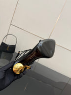Black sandal close-up with glossy finish and gold-tone stiletto heel detail.