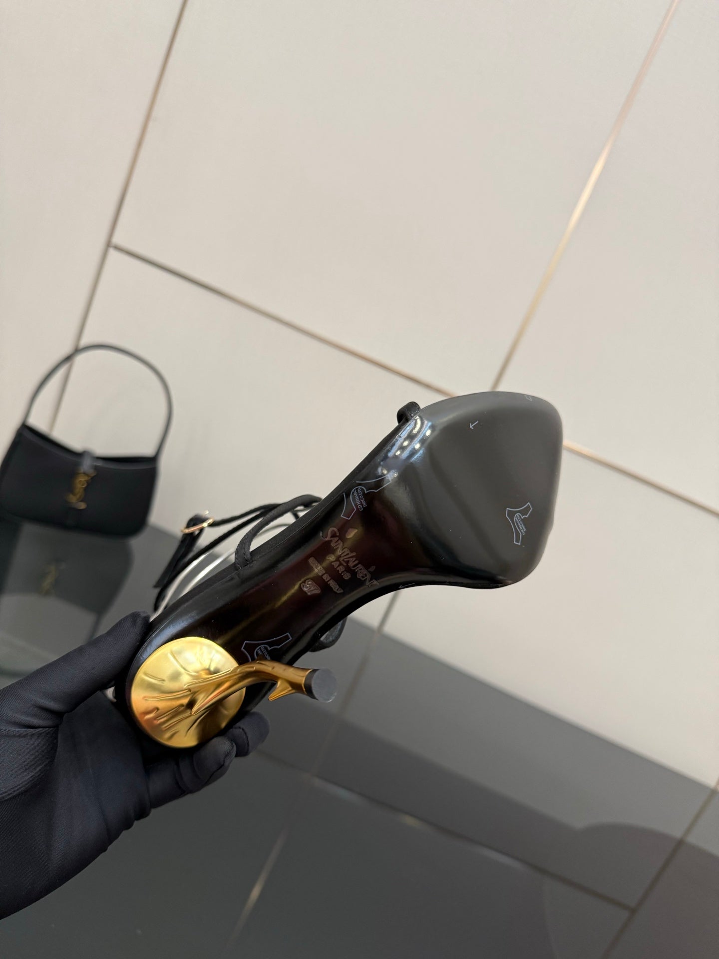 Black sandal close-up with glossy finish and gold-tone stiletto heel detail.