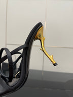 Black strappy sandal with gold-tone curved stiletto heel, close-up side view.