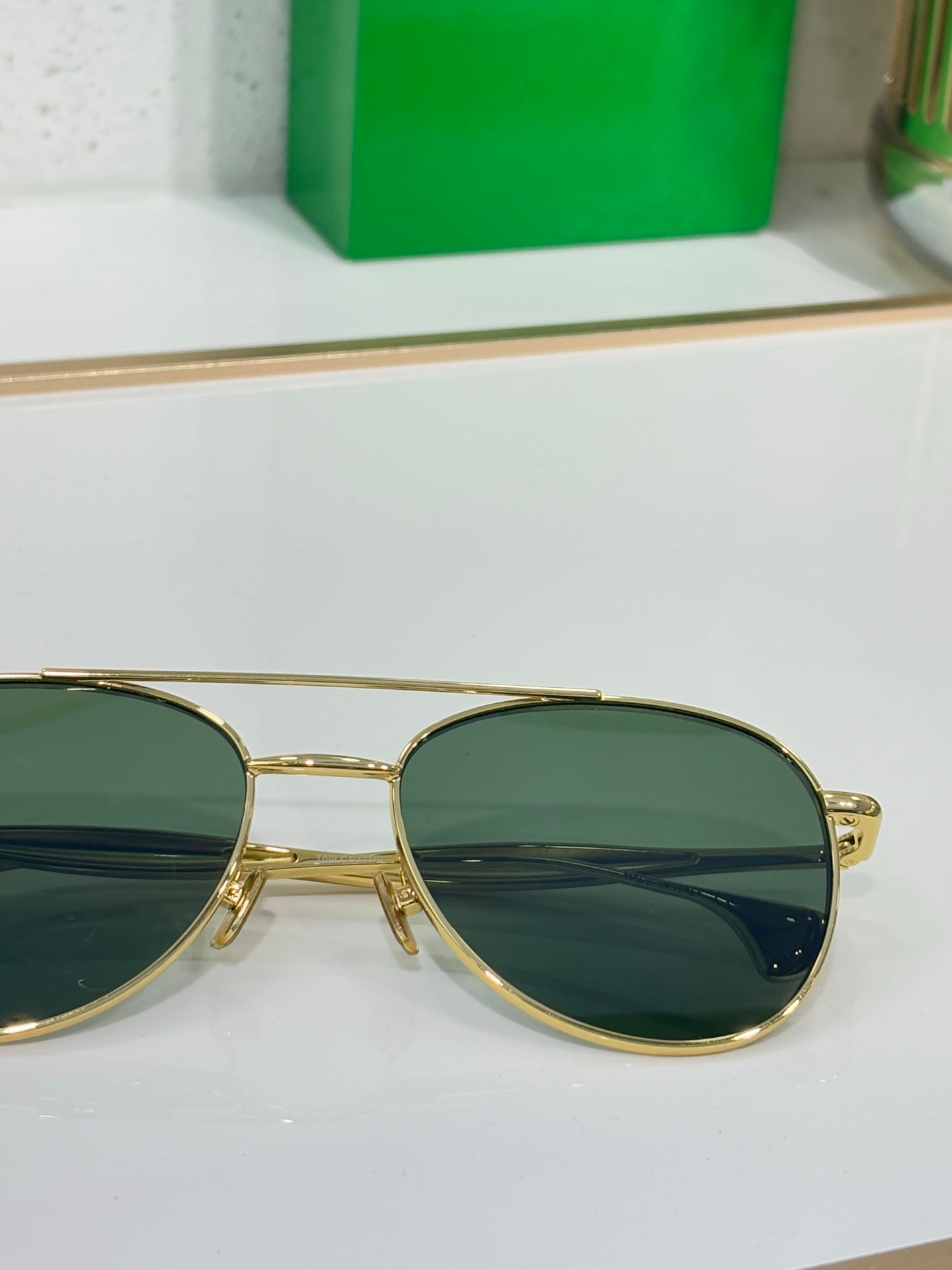 Close-up: round sunglasses with gold frame and dark green tinted lenses.