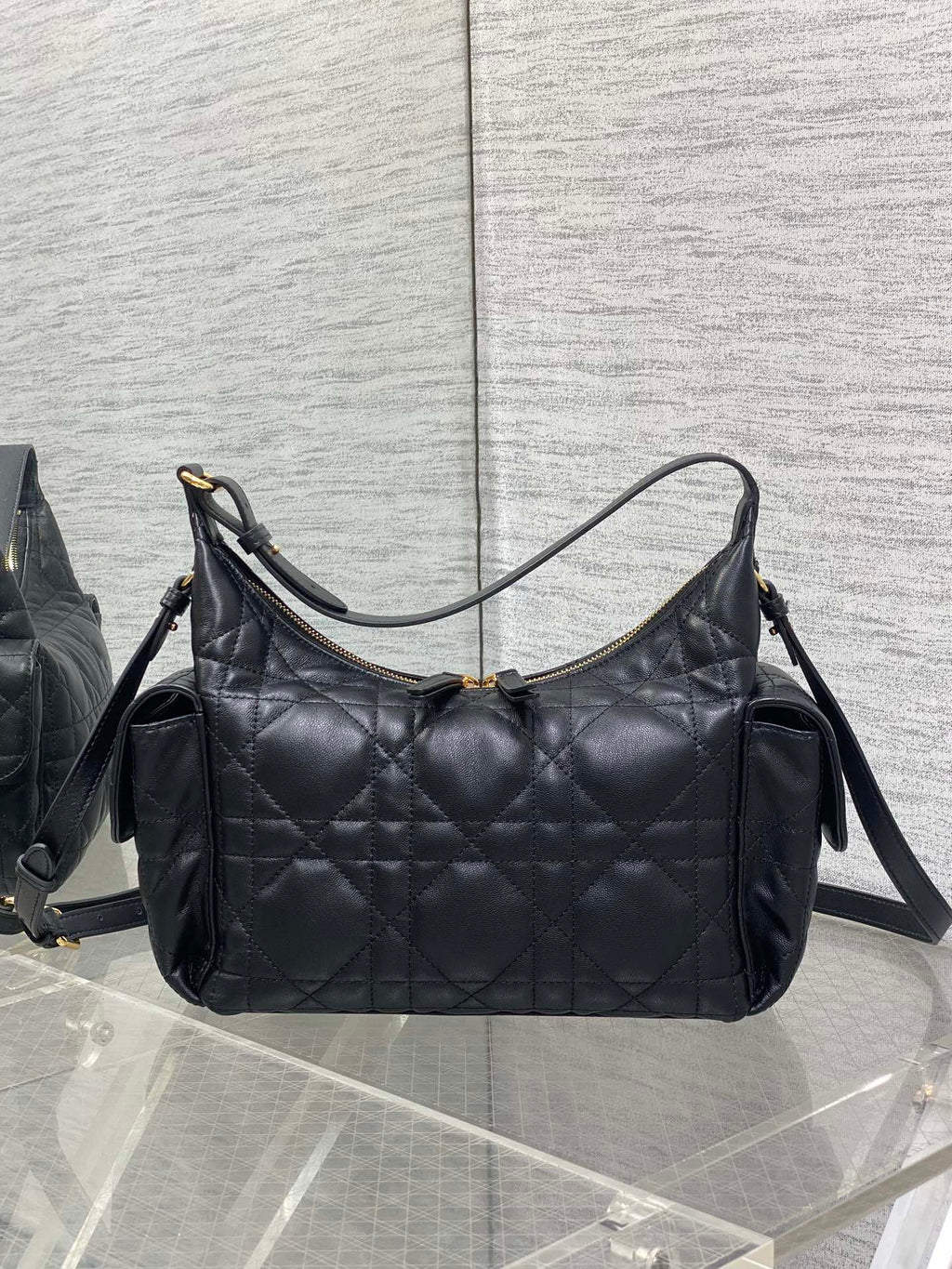 Black quilted shoulder bag with curved top handles, shoulder strap, and gold hardware