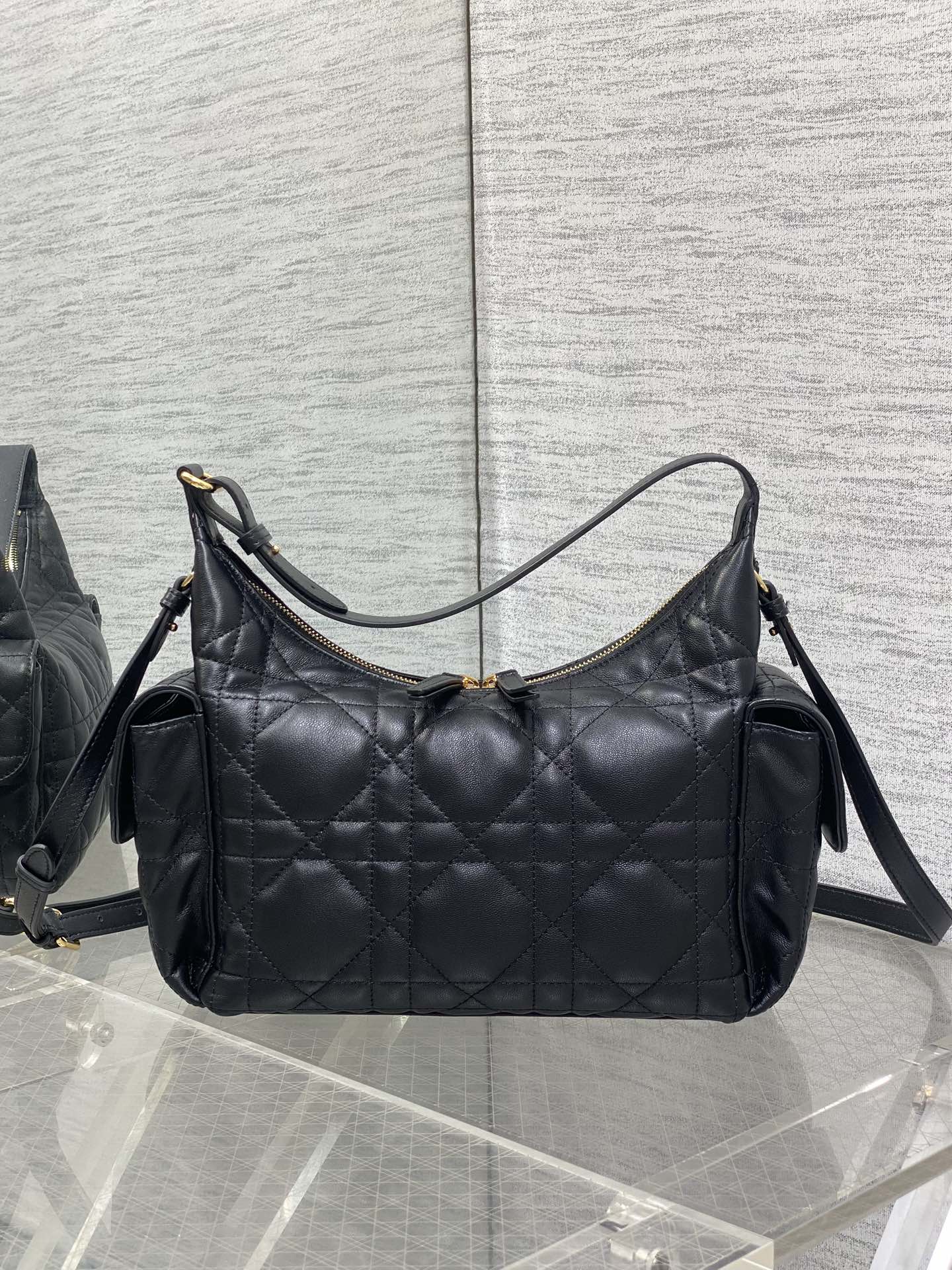 Black quilted shoulder bag with curved top handles, shoulder strap, and gold hardware
