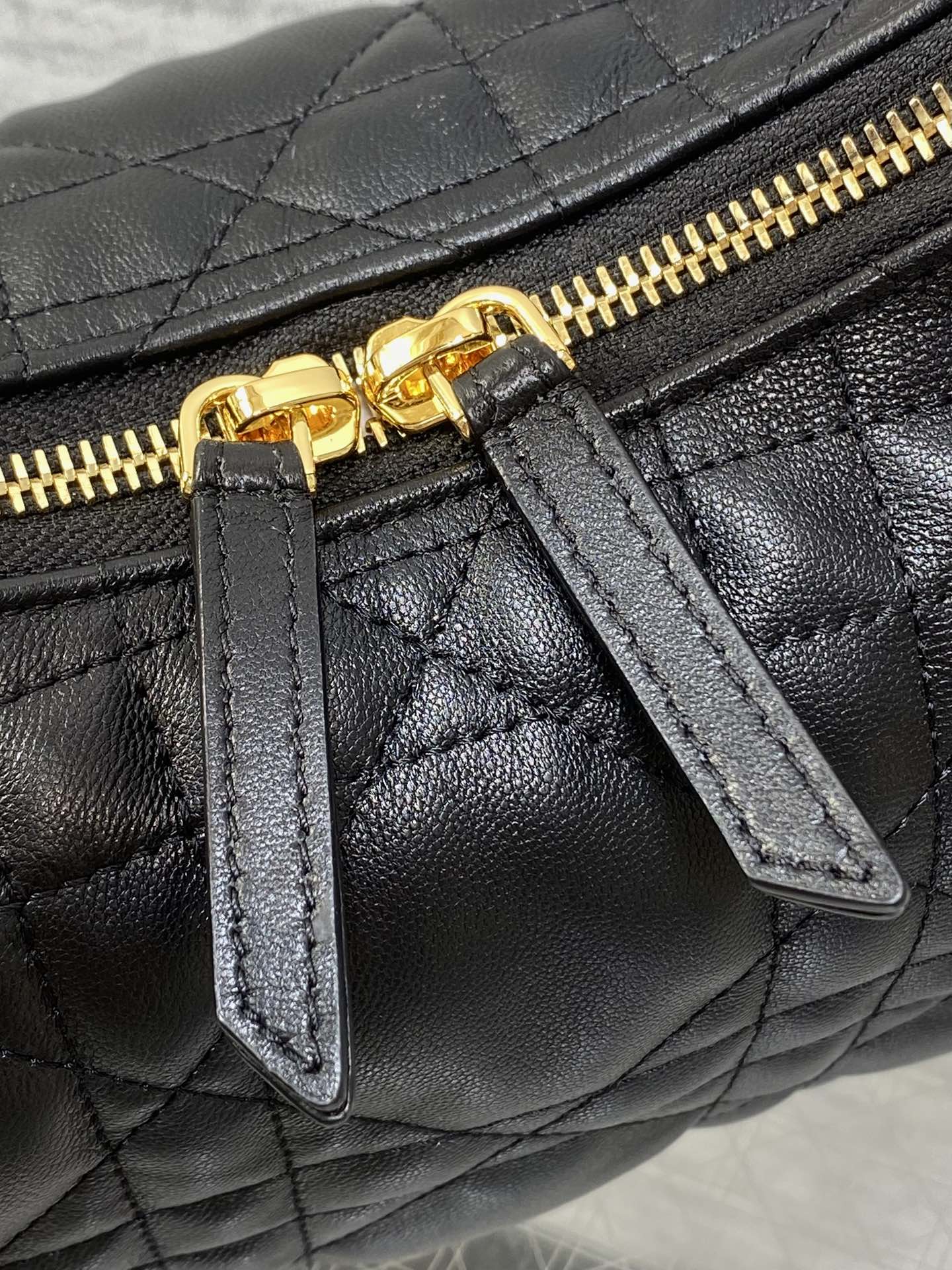 Dior bag detail: gold-tone zipper pull with leather tab on quilted black bag