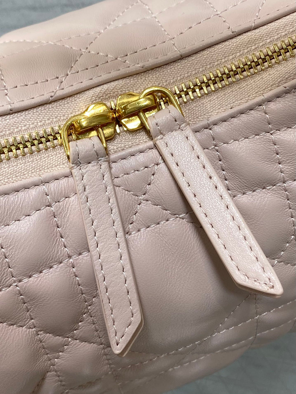 Light pink quilted strap detail with gold zipper pull and leather tab