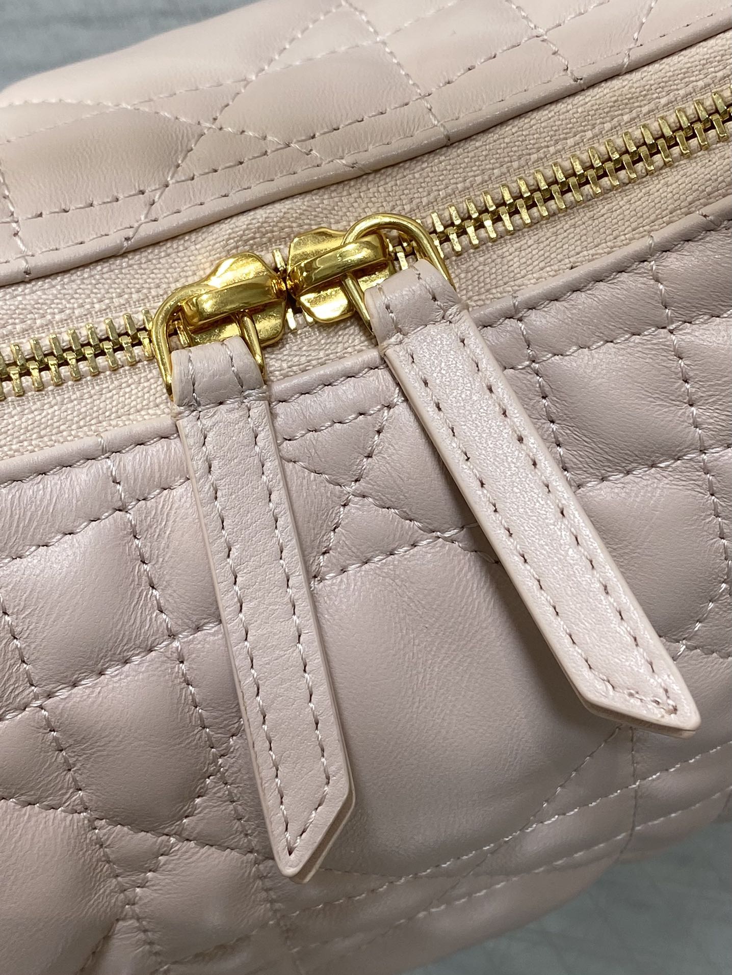 Light pink quilted strap detail with gold zipper pull and leather tab