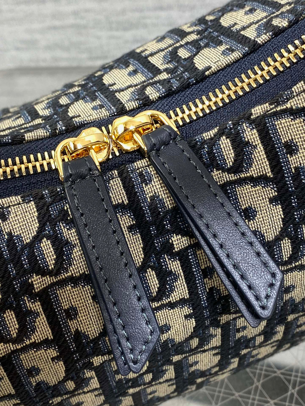 Dior Oblique zip pocket detail with navy leather tab and gold zipper, close-up