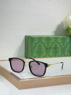 Glasses with black frames, gold accents, and mauve-tinted lenses