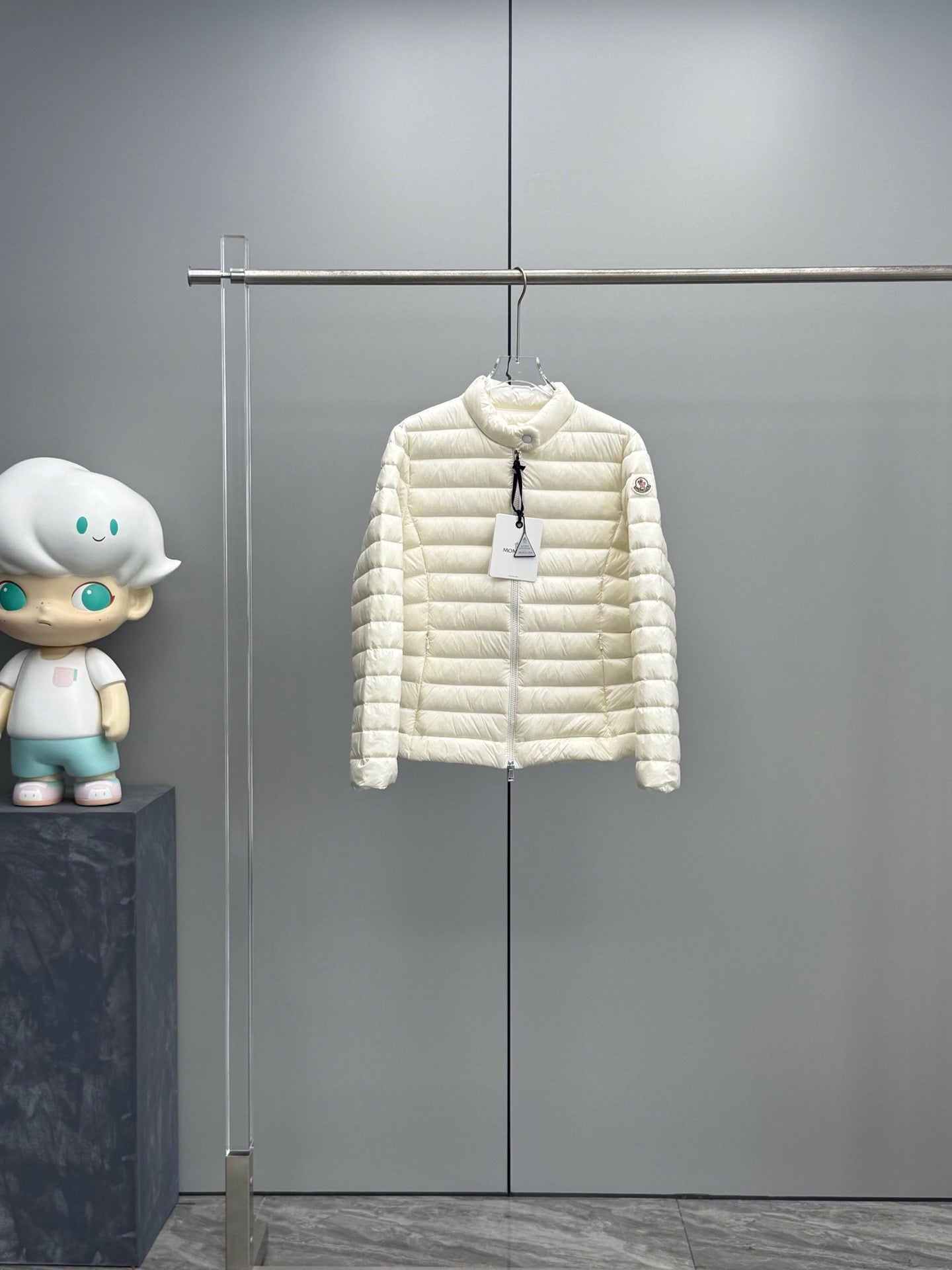 Moncler hooded puffer jacket in light color, front zip closure, hanging on a rack