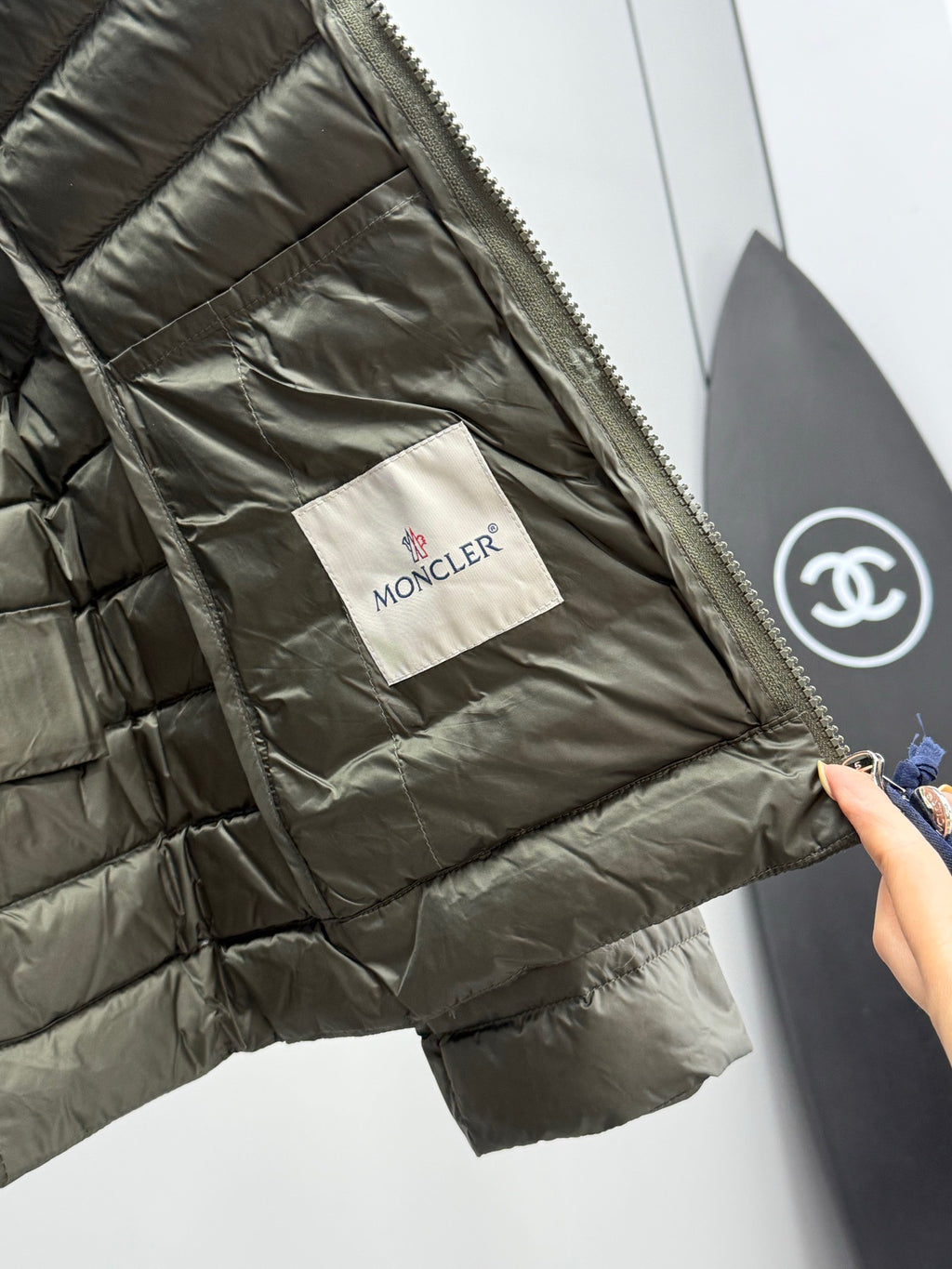 Olive puffer jacket interior with Moncler fabric tag and side seam pocket.