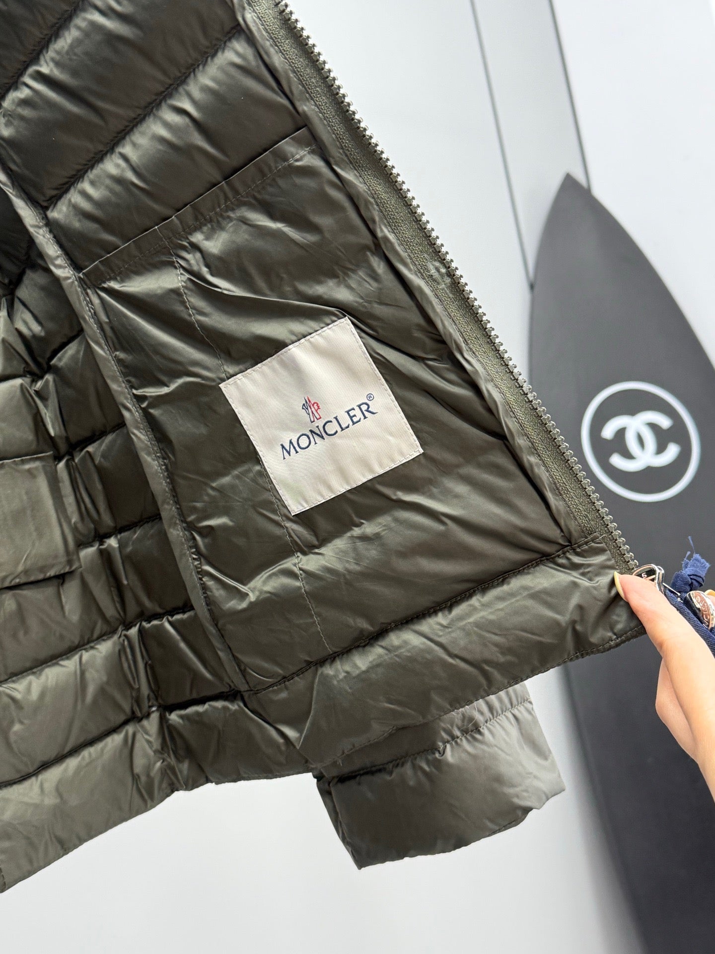 Olive puffer jacket interior with Moncler fabric tag and side seam pocket.