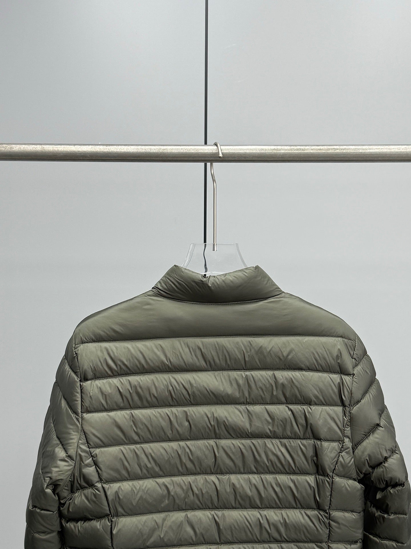 Olive puffer jacket with horizontal quilted stripes and high collar.