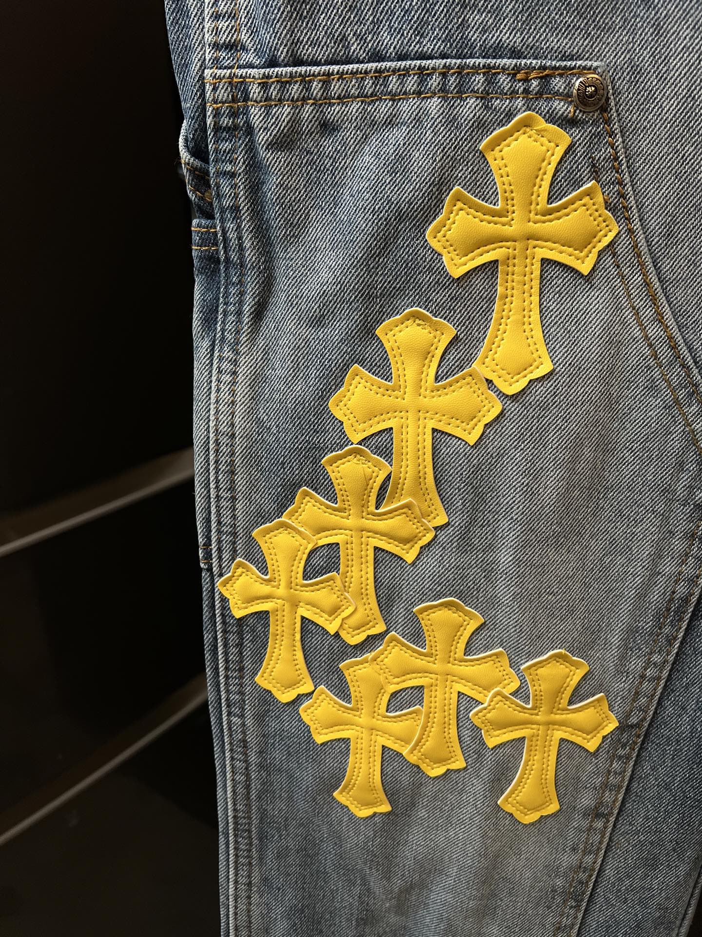 Light blue denim pants with large yellow cross patch on the pocket