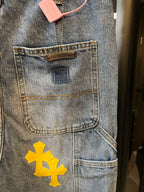 Light blue denim pants with front pocket label and yellow cross patch