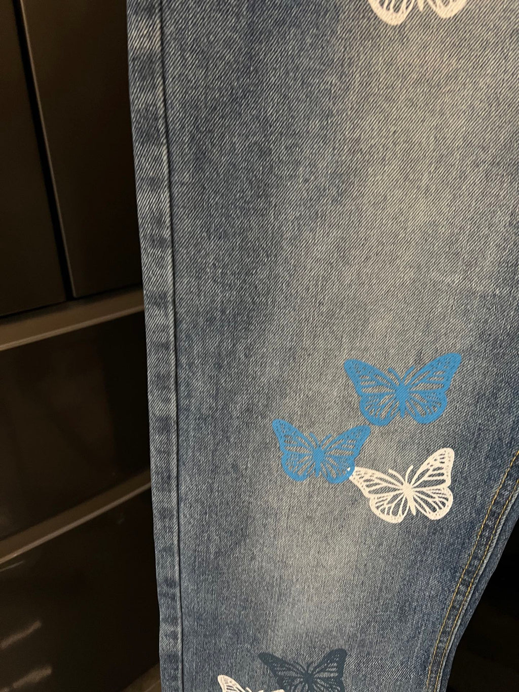 Blue denim pants with butterflies graphic on the leg, cropped side view
