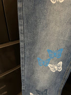 Blue denim pants with butterflies graphic on the leg, cropped side view