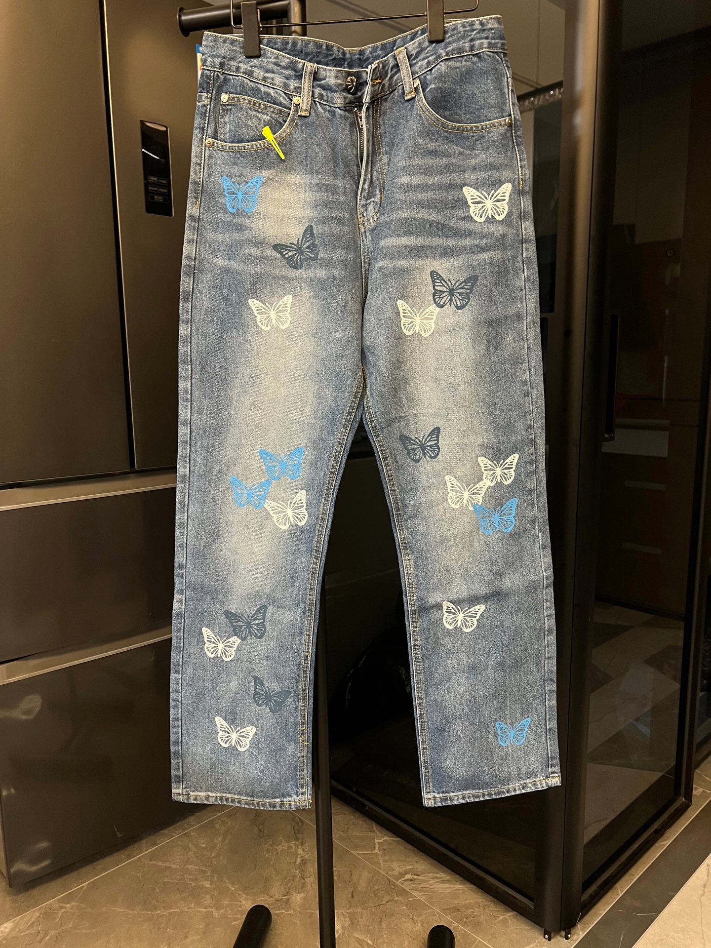 Light blue denim pants with butterfly patches, front zipper, and belt loops